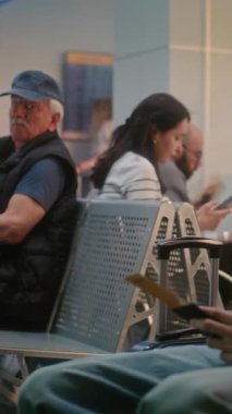 Kalabalık Uluslararası Havalimanı Terminali: Ayrılış Salonunda Çeşitli Yolcuların ve Yolcuların Doli Çekimi. Genç Çocuk Akıllı Telefon Kullanıyor ve Kaydırıyor, Uçak Uçuşunu Bekliyor. Dikey Çekim.