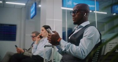 Uluslararası Havalimanı Terminali 'ndeki VIP Gidiş Salonu: Afrika kökenli Amerikalı İşadamı Smartphone' da çalışıyor. Uçak Uçuşunu Bekleyen Dijital Aygıtları kullanan Çeşitli İş Adamları. Doli Vuruşu.