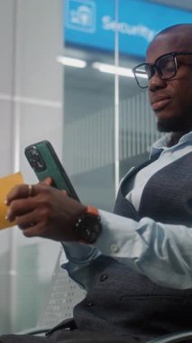Havaalanı Terminali: Afro-Amerikan Girişimci Akıllı Telefon kullanarak uçak bileti tarama, bilgi kontrolü. İşadamı, Kalkış Salonunda Uçuş Bekliyor. E-Bilet Teknolojisi. Dikey Çekim.