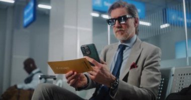 Havaalanı Terminali: Başarılı İşadamı Tarayıcı Uçuş Bilgilerini Kontrol ederek Akıllı Telefon kullanarak Uçuş Geçidi. Olgun Girişimci VIP Ayrılış Salonu 'nda oturuyor. E-Bilet Teknolojisi. Doli Vuruşu.