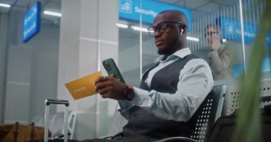 Havaalanı Terminali: Afrikalı Amerikalı Başarılı Girişimci Akıllı Telefon Kullanarak Uçak Biletini Tarıyor, Bilgi Kontrol Ediyor. VIP Ayrılış Salonunda Uçağı Bekleyen İşadamı. E-Bilet Teknolojisi.