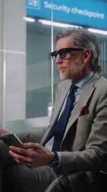 Havaalanı Terminali: Akıllı Telefon Kullanmakta, Kahve İçmekte, Bagajda Oturmakta. Olgun iş adamı uçuşu bekliyor, iş gezisine çıkıyor. Çekim, Dikey Vuruş.