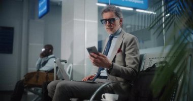 Uluslararası Havaalanı Terminali: Kalkış Salonunda Dizüstü Bilgisayarlı Başarılı Girişimci, Telefonu Kullanıyor. İş adamı uzaktan çalışıyor, uçuşu bekliyor, iş seyahatine çıkıyor. Yavaş Hareket.