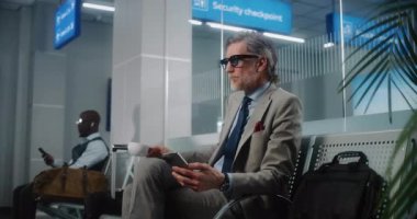 Havaalanı Terminali: Akıllı Telefon Kullanan ve Kahve İçen Başarılı Adam, Gidiş Salonunda Bavulla Oturuyor. Olgun iş adamı uçuşu bekliyor, iş gezisine çıkıyor. Dolly shot, orta boy..