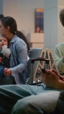 Kalabalık Uluslararası Havaalanı Terminali Kulaklıklı Genç Telefon Kullanıyor, Küçük Bebekle Oturan Kadın. Insanlar ve Yolcular Biniş Salonunda Uçak Uçuşunu Bekliyor. Dikey Çekim.