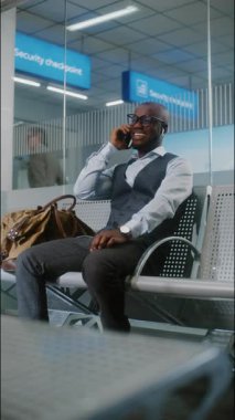Havaalanı Terminali: Başarılı Afrikalı Amerikalı İş Adamı Cep Telefonu ile İş Ortağıyla Konuşuyor. Girişimci, Airline Hub 'ın Kalkış Salonunda Uçuşu Bekliyor, Seyahate Çıkıyor. Dikey Çekim.