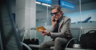 Havaalanı Terminali: Ciddi İşadamı Smartphone konuşuyor, Uçuş bilgilerini kontrol ediyor, uçak biletini tutuyor. Başarılı Olgun Adam Ayrılış Salonu 'nda oturuyor, iş gezisine çıkıyor. Yavaş Hareket.