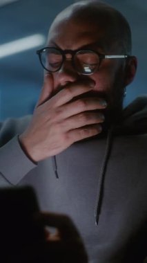 Kalabalık Uluslararası Havaalanı Terminali: Yorgun ve Uykulu Adam Esneme, Dijital Tablet Kullanırken Uyuklama. Yolcu Geceleyin Yatılı Salonda, Gecikmeli Uçuşu Bekliyor. Dikey Çekim