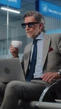 Havaalanı Terminali: Başarılı İşadamı Laptop Kullanıyor ve Kahve İçiyor, E-posta gönderiyor. Girişimci Çevrimiçi Çalışan Ayrılış Salonunda Uçuş Bekliyor. Ağır çekim. Dikey Çekim.