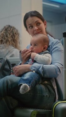 Kalabalık Uluslararası Havaalanı Terminali: Küçük Kollu Yetişkin Kadın Oturuyor ve Seyahat İçin Uçak Bekliyor. Yatılı Salon 'da çeşitli insanlar ve yolcular var. Dikey Çekim.