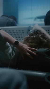 Kalabalık Uluslararası Havaalanı Terminali: Yorgun Bir Kadın Geceleyin Yatılı Salonda Sırt Sırtında Uyuyor. Çeşitli İnsanlar ve Yolcular Gecikmiş Uçak Uçuşunu Bekliyor. Dikey Çekim.