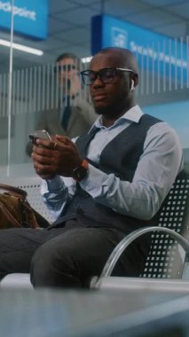 Havaalanı Terminali: Afrikalı Amerikalı İşadamı Akıllı Telefon Kullanıyor, E-İş Yapıyor. Erkek Girişimci Ayrılış Salonunda Uçak Uçuşunu Bekliyor, İş Gezisine Gidiyor. El bilgisayarı. Dikey Çekim.