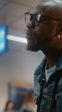 Kalabalık Uluslararası Havaalanı Terminali: Afro-Amerikan Adam Burger Yiyor ve Akıllı Telefon Kullanıyor Yatılı Salonda Oturuyor. Gecikmeli uçuş bekleyen yolcu. Orta boy yakın çekim. Dikey Çekim.