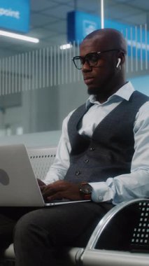 Havaalanı Terminali 'ndeki VIP Gidiş Salonu: Laptop' ta iş yapan Afrikalı Amerikalı İşadamı. Uçuşu Bekleyen Dijital Gadget 'larla çalışan çok ırklı iş adamları. Dolly Shot. Dikey Çekim