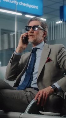 Havaalanı Terminali: Cep telefonuyla konuşan kendinden emin iş adamı, kalkış salonunda oturuyor. Başarılı Girişimci Uçak Uçuşunu Bekliyor, İş Gezisine Çıkıyor. Dolly Shot. Dikey Çekim.