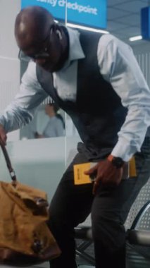 Uluslararası Havaalanı Terminali: Çantalı Afro-Amerikan İşadamı Akıllı Telefon Kullanıyor, İş Gezisine Gidiyor. Girişimci Uçuşu Bekliyor, Ayrılış Salonunda Oturuyor. Ağır çekim. Dikey Çekim