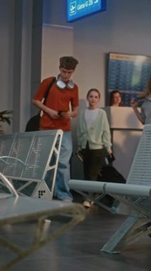 Kalabalık Havaalanı Terminali: İki Genç Çocuklu Kadın ve Pasaport Kontrolünden Sonra Kalkış Salonunda Oturan Kadın, Uçuşu Bekliyor. Güvenlik kontrolünde bekleyenler kuyruğunda. Dikey Çekim.