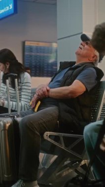 Kalabalık Uluslararası Havaalanı Terminali: Uçuşlar ve Seyahatler için Yolcu Kapısına Yürüyen çeşitli Yolcular. Bagajda Uyuyan Kıdemli Adam Ayrılış Salonunda Koltukta Oturuyor. Dikey Çekim.