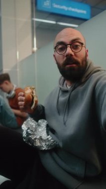 Havalimanı Terminali: Popüler Blogger, Influencer Vlog from Trip using Smartphone, Seating Burger, Sitting on the Floor in Departure Lounge. Seyahat Blog 'u için video içeriği, video çağrısı. Dikey Çekim