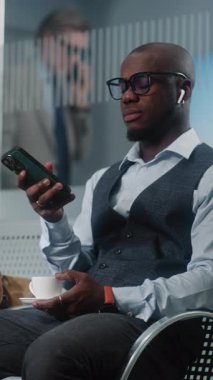 Havaalanı Terminali: Akıllı Telefon Kullanımı ve İçme Kahvesi ile Başarılı Girişimci. Afrika kökenli Amerikalı iş adamı, kalkış salonunda uçak bekliyor, iş gezisine çıkıyor. Yavaş Hareket, Dikey Çekim.