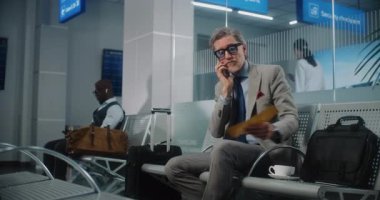 Uluslararası Havaalanı Terminali: Ciddi Girişimci, Gecikmeli Uçuş Konuşmasının Telefonda Konuşması, Uçak Biletini Tutması Hakkında Sinirlendi. Başarılı İşadamı Ayrılış Salonunda Oturuyor, İş Gezisine Çıkıyor.