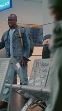 Kalabalık Uluslararası Havaalanı Terminali: Biniş Salonundaki Çeşitli Yolcular ve Yolcular. Bavullu Afro-Amerikan Adam. Akıllı telefon kullanarak uçağın kalkmasını bekliyor. Dikey Çekim.