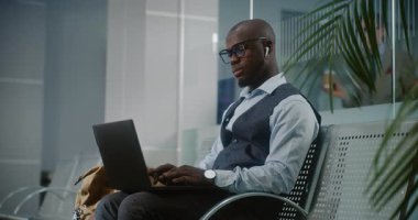 Uluslararası Havalimanı Terminali: Laptop ve Smartphone kullanan Afro-Amerikan İşadamı, İçen Kahve, İnternette Çalışan. Girişimci Ayrılış Salonunda Uçuş Bekliyor. Dolly shot, orta boy.