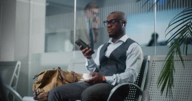 Havaalanı Terminali: Akıllı Telefon Kullanımı ve İçme Kahvesi ile Başarılı Girişimci. Afrika kökenli Amerikalı iş adamı, kalkış salonunda uçak bekliyor, iş gezisine çıkıyor. Yavaş Hareket, Orta Çekim.