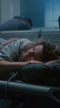 Kalabalık Uluslararası Havaalanı Terminali: Yorgun Kadın Geceleyin Yatılı Salonda Sırt Sırtında Uyuyor. Çeşitli Yolcular ve Turistler Gecikmiş Uçak Uçuşunu Bekliyor. Dikey Çekim.