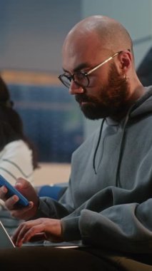 Kalabalık Uluslararası Havaalanı Terminali: İnternette Çalışan Girişimci, E-İş Yapıyor, Uçuşu Bekliyor. Dijital cihazları kullanarak, Ayrılış Salonunda oturan çeşitli insanlar. Dikey Çekim.