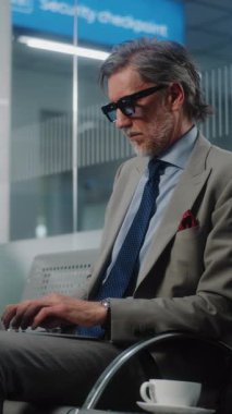 Havaalanı Terminali: Laptop ve Smartphone kullanan başarılı iş adamı, e-posta gönderiyor. Olgun Girişimci Çevrimiçi Çalışan Ayrılış Salonunda Uçuş Bekliyor. Ağır çekim. Dikey Çekim.