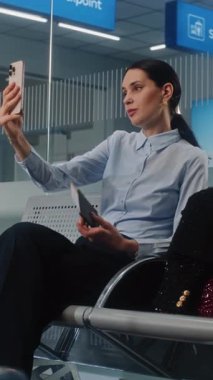 Havaalanı Terminali: Akıllı Telefondan Yatırımcıyla Konuşan Kadın Girişimci, Video Sohbeti. Başarılı bir iş kadını kalkış salonunda uçak bileti bekliyor, iş seyahatine çıkıyor. Dikey Çekim.