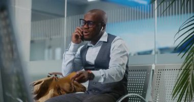 Havaalanı Terminali: Afro-Amerikalı İşadamı Gecikmeli Uçuş Tutma Uçak Biletine Kızmış, Akıllı Telefon 'da Konuşuyor. Girişimci Ayrılış Salonu 'nda oturuyor, iş gezisine çıkıyor. Sabit Çekim.