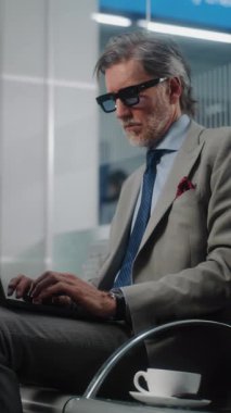 Havaalanı Terminali: Laptop Kullanımı ve İçme Kahve Kullanımı, E-İş Yapımı Başarılı Girişimci. Olgun İşadamı Uzaktan Çalışması Çevrimiçi Ayrılış Salonunda Uçuş Bekliyor. Ağır çekim. Dikey Çekim.