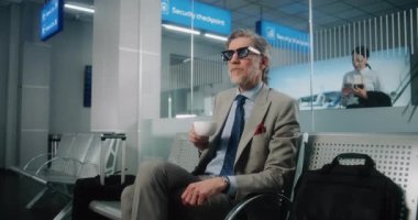 Uluslararası Havalimanı Terminali: Başarılı Adam Bavul Salonunda Bavulla Oturuyor, Kol saatine bakıyor, Kahve içiyor. İş adamı uçuşu bekliyor, iş gezisine çıkıyor. Doli Vuruşu.