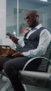 Havalimanı Terminali: Akıllı Telefon Kullanarak Başarılı Adam, Havayolu Merkezinin Kalkış Salonunda Uçuş Bekliyor. Afrika kökenli Amerikalı iş adamı iş gezisine çıkıyor. Ağır çekim. Dikey Çekim.