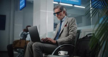 Uluslararası Havalimanı Terminali: Laptop Kullanımı ve İçme Kahve Kullanımı, E-İş Yapımı Başarılı Girişimci. Olgun İşadamı Uzaktan Çalışması Çevrimiçi Ayrılış Salonunda Uçuş Bekliyor. Yavaş Hareket.
