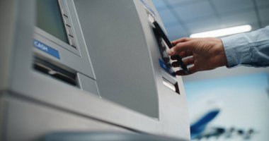 Havalimanı Terminalinde Para Makinesi: Bilinmeyen Kişi Akıllı Telefonu Temassız Para Çekme İşlemi için NFC Okuyucusuna Koyuyor, ATM 'deki Düğmelere Basıyor. Banka hizmetleri. Görüntüyü Kapat.