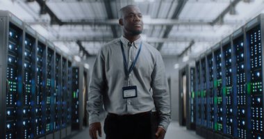 Sunucu Raflı Büyük Veri Merkezi: Tablet Bilgisayar Deposunda Yürüyen Profesyonel Afro-Amerikan Uzmanı. İnternet Sunucuları, Bilgi Teknolojisi, Siber Güvenlik ve Haberleşme.