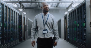 Sunucu Raflı Büyük Veri Merkezi: Tablet Bilgisayar Deposunda Yürüyen Profesyonel Afro-Amerikan Uzmanı. İnternet Sunucuları, Bilgi Teknolojisi, Siber Güvenlik ve Haberleşme.