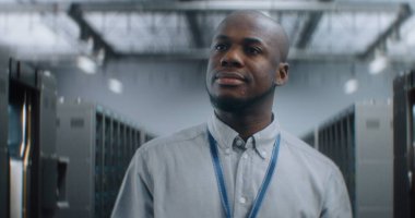 Profesyonel Afrikalı Amerikalı Uzman, Yönetici Sunucu Raflarıyla Büyük Veri Merkezi 'nde Yürüyor, Gülümsüyor, Kameraya Bakıyor. İnternet Sunucuları, Bilgi Teknolojisi ve Siber Güvenlik Konsepti.