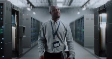 Sunucu Raflı Büyük Veri Merkezi: Tablet Bilgisayar Deposunda Yürüyen Profesyonel Afro-Amerikan Uzmanı. İnternet Sunucuları, Bilgi Teknolojisi, Siber Güvenlik ve Haberleşme.