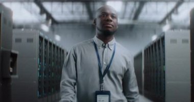 Profesyonel Afro-Amerikan Yönetici, Sunucu Raflarıyla Büyük Veri Merkezi 'nde Yürüyen Uzman, Gülümseyen, Kameraya Bakan. İnternet Sunucuları, Bilgi Teknolojisi, Siber Güvenlik. Dolly Yakınlaştır.