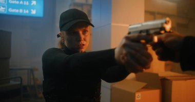 Action Movie Scene: Siyah Taktik Giyimli Kadın Polis Memuru ve Depoda Kaptan Yürüyor, Silah Tutuyor, Tabancalı Bilinmeyen Suçluyu Buluyor. Karanlık Bina 'da Saldırgan Ajan