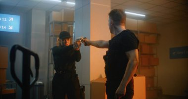 Silahlı Karşılaşma: Taktik Ekipmandaki Kadın ve Adam Birbirlerine Silahlar Nişan alıp Konuşuyorlar. Karanlık Depo veya Depo 'da Subay Suçluya Saldırıyor. Gerginlik ve Aksiyon Filminden Dramatik Sahne.