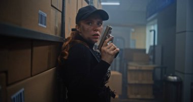 Siyah Taktik Ekipman 'daki Kadın Gizli Ajan ve Depo' da Saklanan Kaptan, Silah Tutan, Katille Konuşan. Memur Karanlık Depo Tesisinde Suçlu 'ya saldırmaya ya da tutuklamaya hazırlanıyor. Eylem Filmi Sahnesi