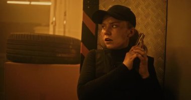 Taktik Ekipman Deposu 'nda gizlenen, elinde silah tutan, Katille konuşan gizli bir kadın ajan. Memur Karanlık Depo Tesisinde Suçlu 'ya saldırmaya ya da tutuklamaya hazırlanıyor. Aksiyon Film Sahnesi. Sıcak. Bak..