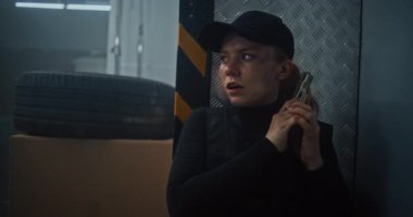 Siyah Taktik Ekipman 'daki Kadın Gizli Ajan ve Depo' da Saklanan Kaptan, Silah Tutan, Katille Konuşan. Memur Karanlık Depo Tesisinde Suçlu 'ya saldırmaya ya da tutuklamaya hazırlanıyor. Eylem Filmi Sahnesi