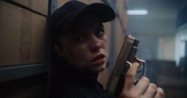 Taktik Ekipman 'daki Kadın Gizli Ajanın Kapağı Gizleniyor, Bir Tabanca Tutuyor, Katille Konuşuyor. Memur Karanlık Depo 'da Suçlu' ya saldırmaya ya da tutuklamaya hazırlanıyor. Epic Action Film Sahnesi.