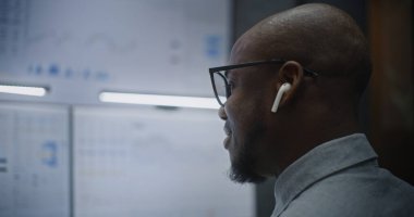 Kablosuz kulaklık takan borsa simsarı, Gerçek zamanlı hisse senedi takibini takip eden, çoklu-monitör kurulumunda borsa grafikleri değiştiren. Afrika kökenli Amerikalı Yatırım Ajanı. Kapat.